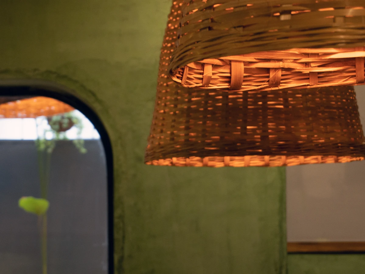 Srashtea Caf&eacute; — a woven cane pendant lit against a green lime-plastered wall